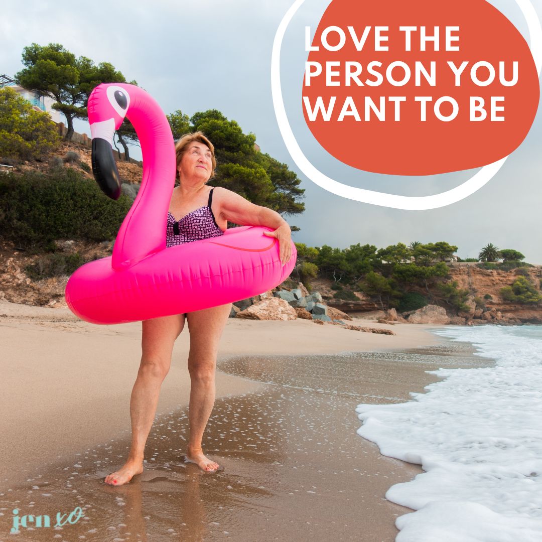 An older woman in a swim suit standing on a beach with a giant flamingo floaty around her middles and an orange circle with the words Love The Person You Want to Become
