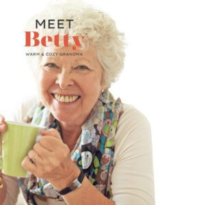 A lovely older woman smiling at the camera with a coffee mug in her hand and the words Meet Betty - Warm & Cozy Grandma